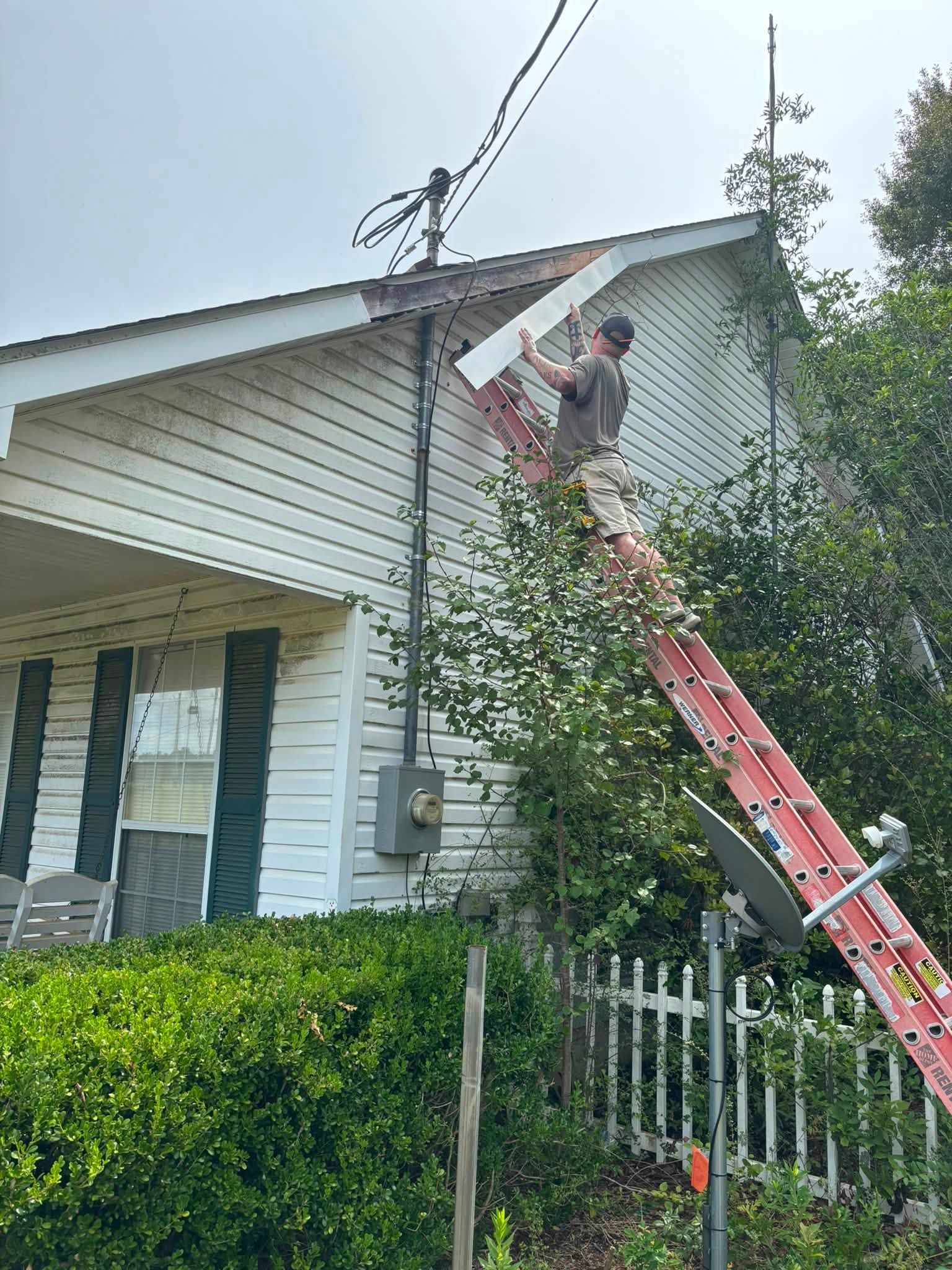 REDLINE on a ladder fitting new fascia board at the peak of a gable