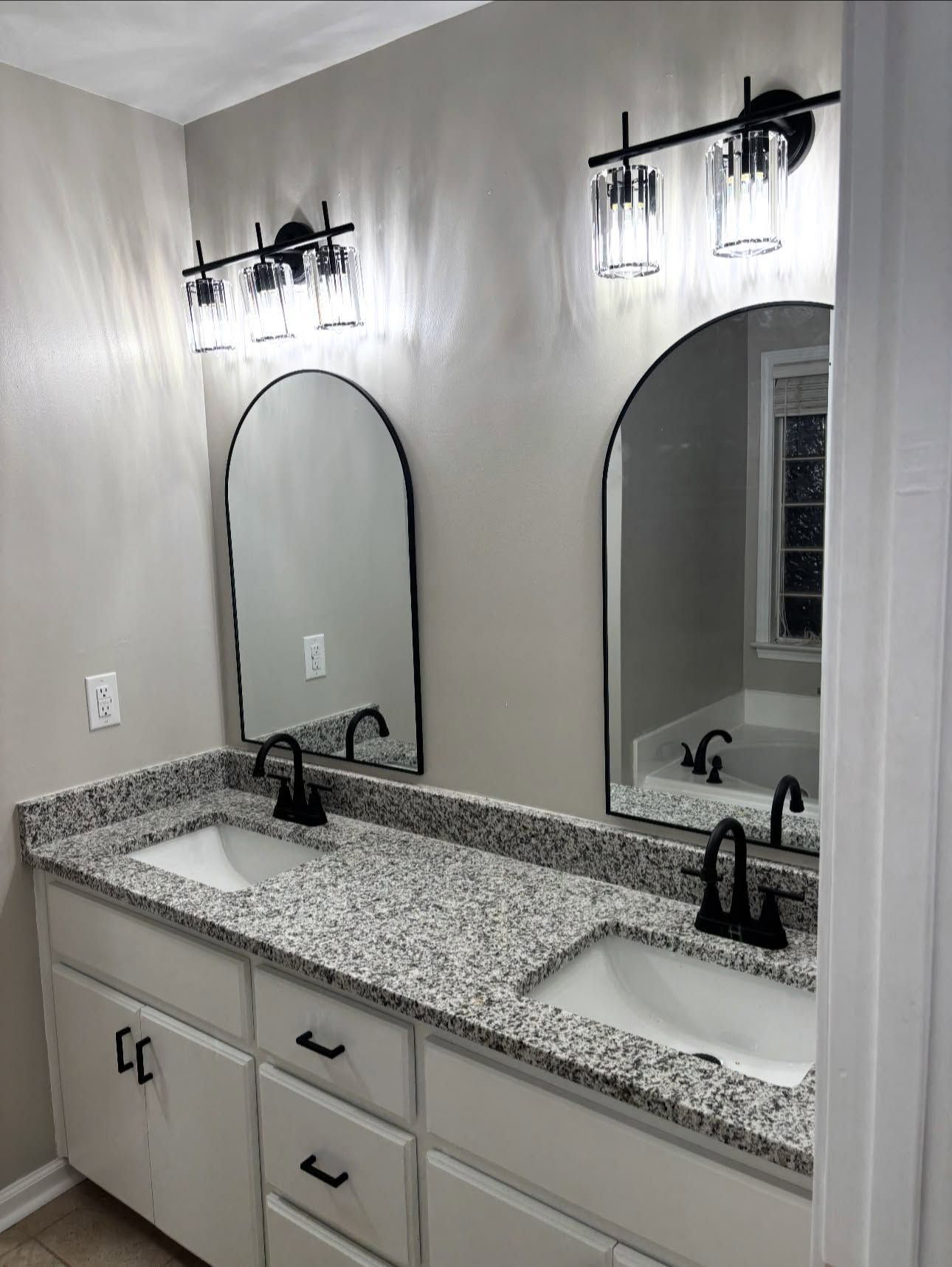 After: repainted double vanity with black hardware, two arched black-framed mirrors and new glass light bars
