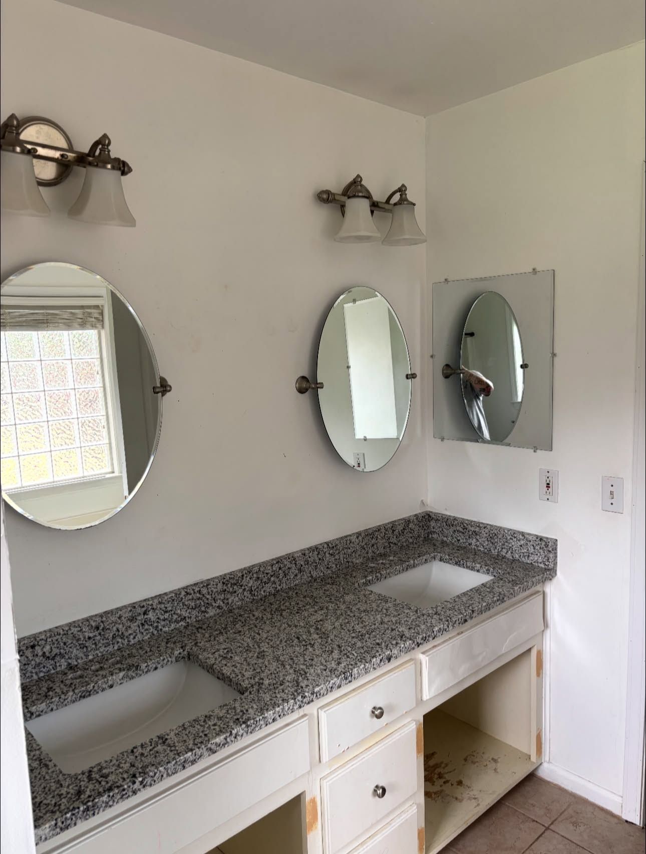 Before: double vanity with granite top, three oval mirrors and dated wall sconces