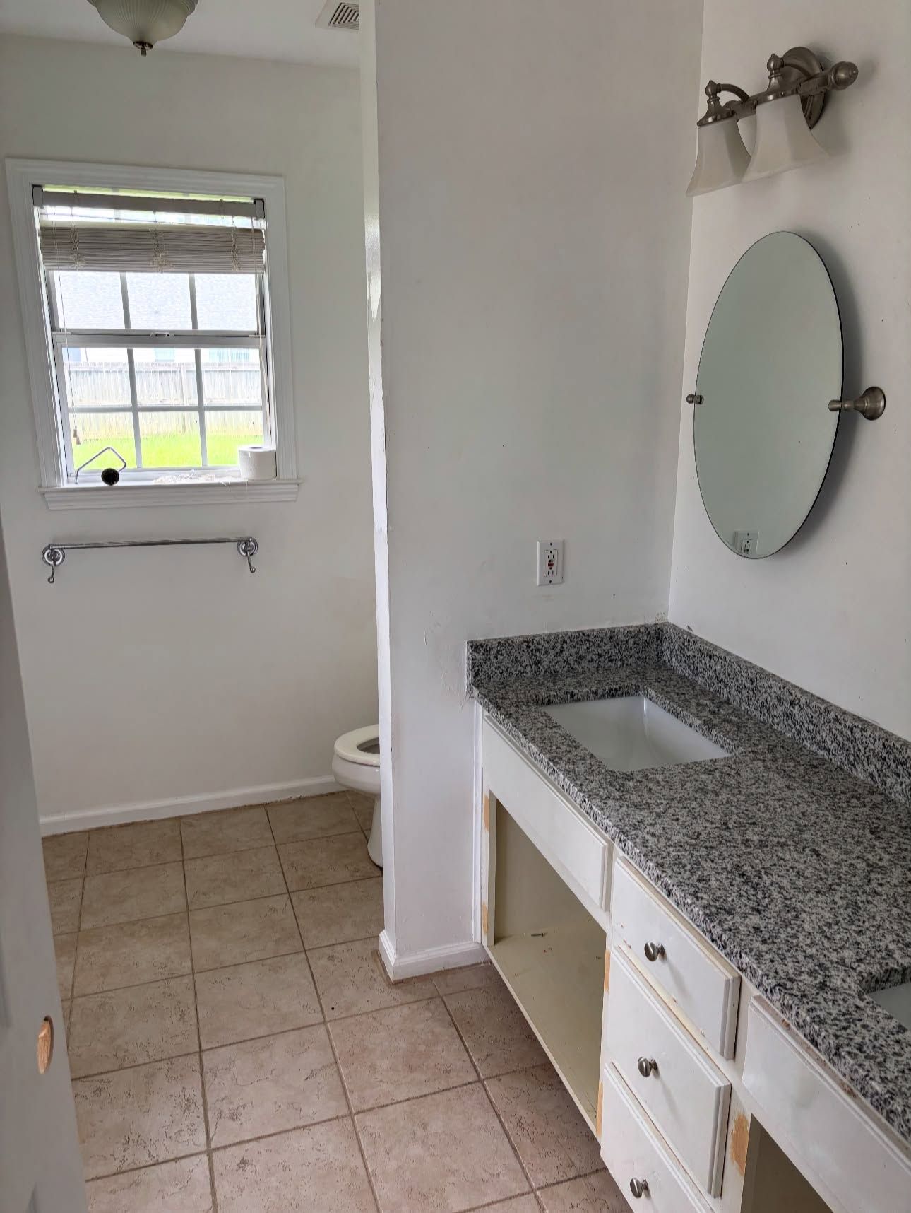 Bathroom before: white vanity with a missing cabinet door, oval mirrors and older brass light fixtures