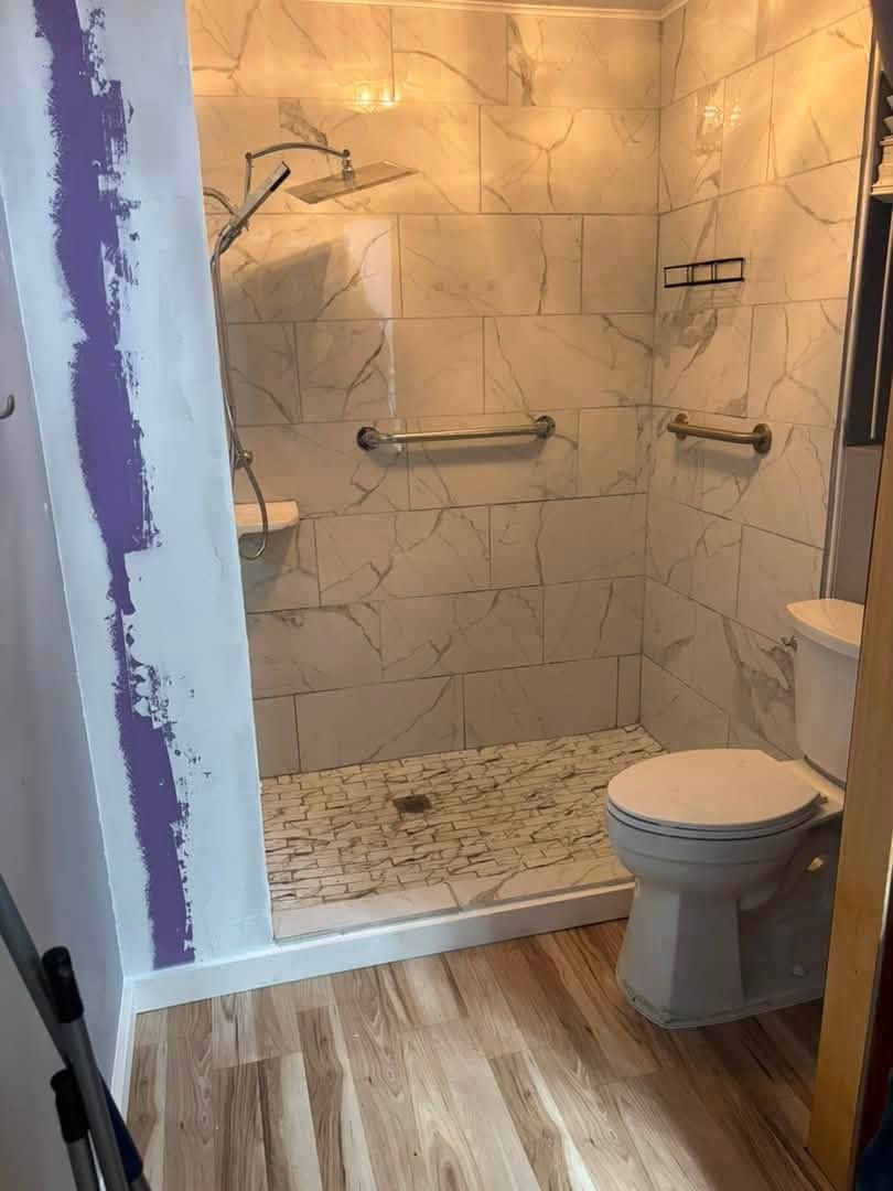 Walk-in shower with large marble-look wall tile, pebble floor and grab bars