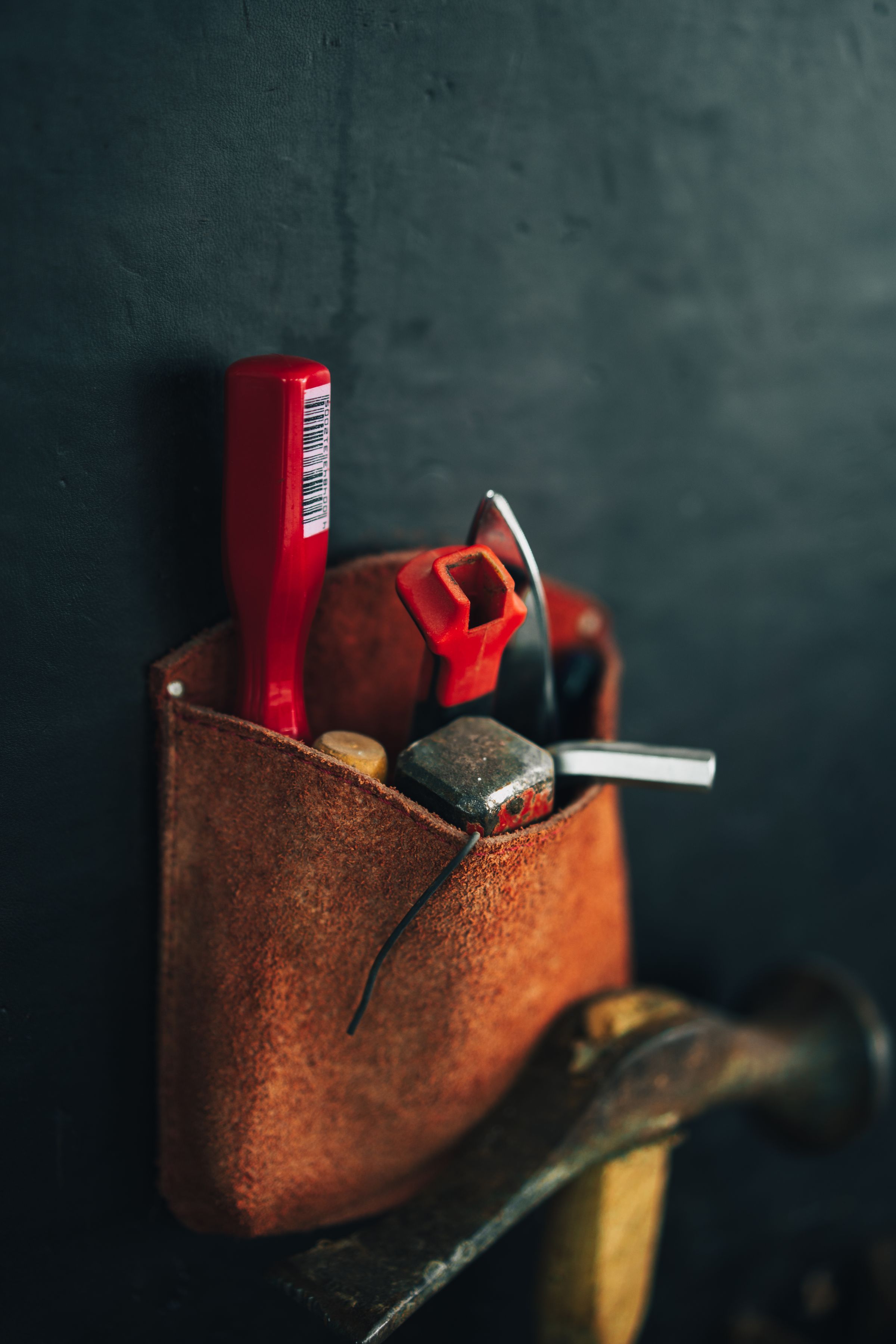 Leather tool pouch with a hammer and pliers hanging on a dark wall