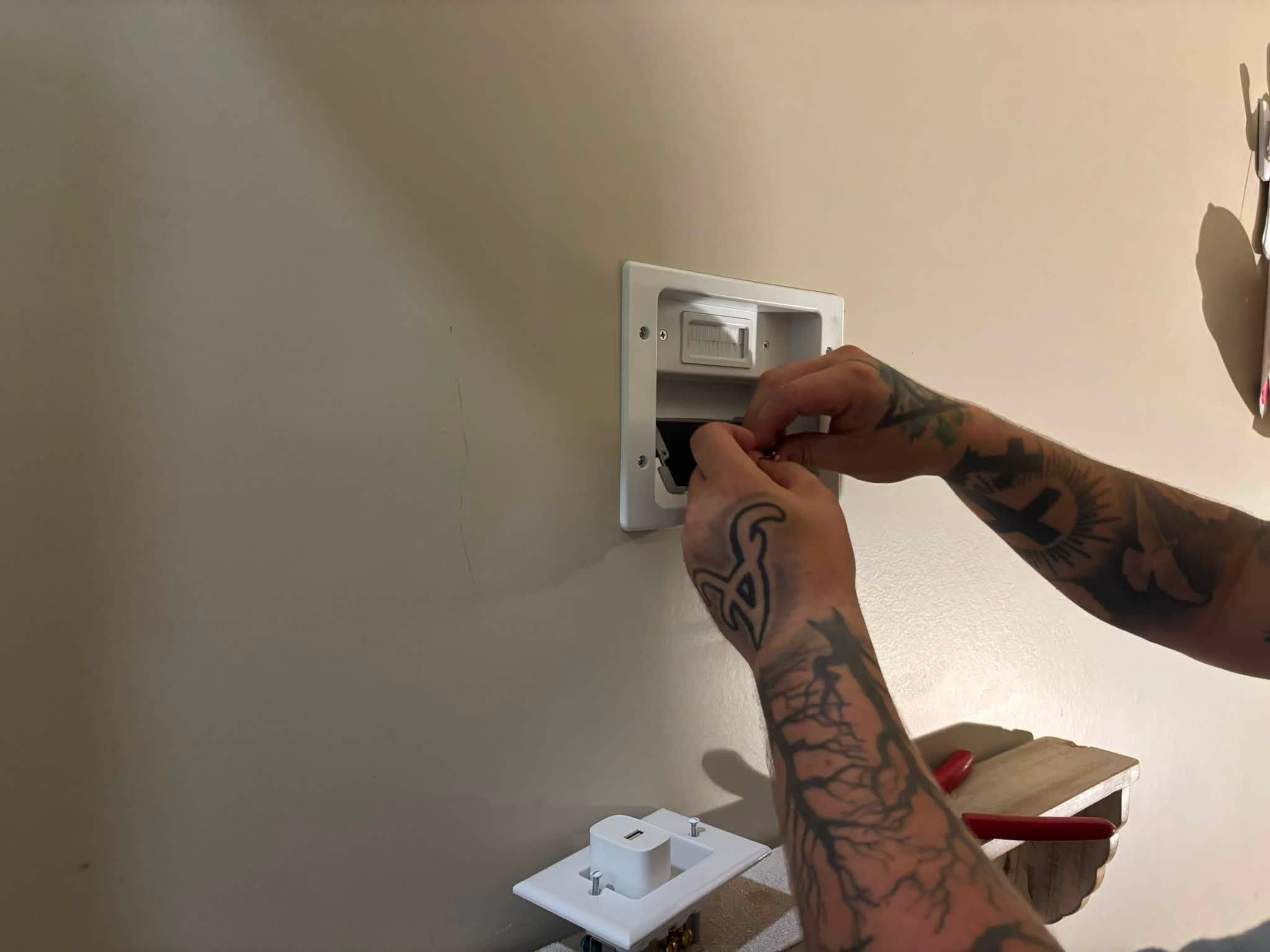 Hands fitting a recessed power and cable plate into the wall